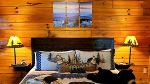 Ein gemütliches Zimmer mit Holzwänden, einem Bett mit gesteppter Decke, zwei Nachttischen mit Lampen und einem Wandbild.