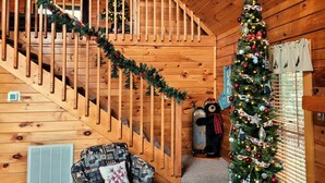 Ein gemütliches Blockhaus-Interieur mit einer Holztreppe, einem Weihnachtsbaum und einer Bär-Dekoration.