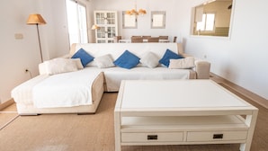 A modern bedroom with a large bed, a bedside table, and a small table. There is a window with blinds, a lamp, and a mirror on the wall. - HAYMAN II          . (Ventorros de San José)
