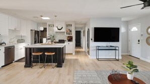 A modern kitchen with a central island, bar stools, and a dining area with a TV.