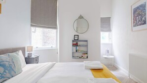 Ein Schlafzimmer mit Bett, Nachttisch, Lampe, Bücherregal und Heizkörper.