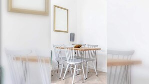 Ein Essbereich mit Holztisch und weißen Stühlen, einem gerahmten Bild an der Wand und einer Lampe.