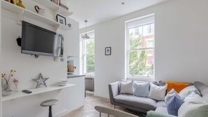 Ein modernes Wohnzimmer mit grauem Sofa, einem flachbildfernseher an der Wand und einem großen Fenster, das für natürliches Licht sorgt.