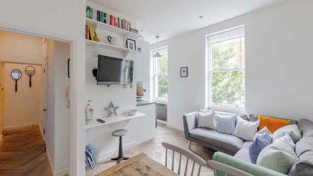 Ein modernes Wohnzimmer mit einem grauen Sofa, einem Holztisch und einem an der Wand befestigten Fernseher.