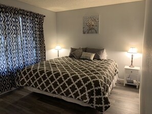 A bedroom with a patterned bedspread, two bedside lamps, a nightstand, and a wall-mounted picture.