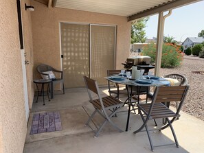 An outdoor patio with a table set for dining, chairs, a grill, and a sliding glass door.
