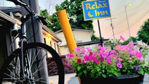 A bicycle leaning against a building, a potted plant with flowers, and a sign that reads "Relax Inn".