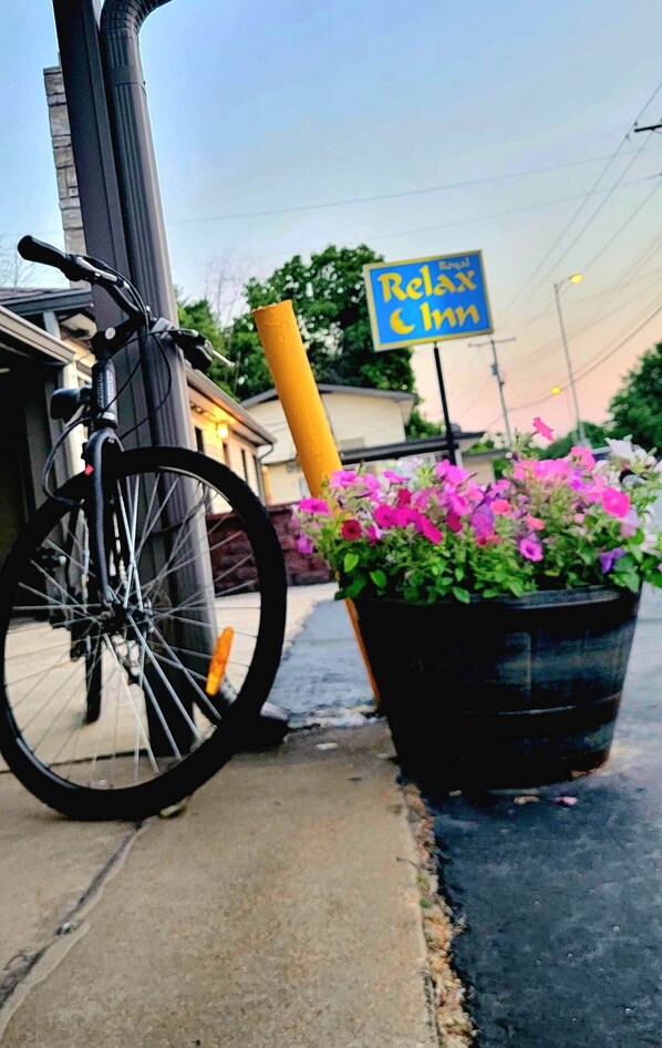 Uma bicicleta encostada em um edifício, um vaso de plantas com flores e uma placa com a inscrição 'Relax Inn'.