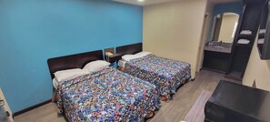 Quarto de hotel com duas camas, uma mesa de cabeceira, um espelho e banheiro com pia e porta-toalhas.