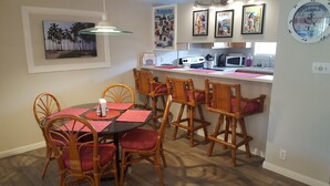 A dining area with a round table, six wooden chairs, and a kitchen in the background.
