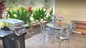 An outdoor patio with a grill, dining table, and chairs.