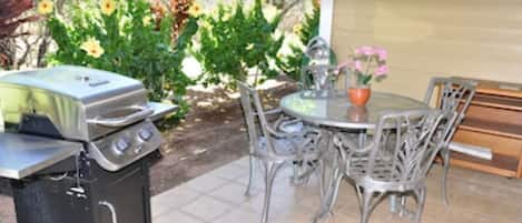 An outdoor patio with a grill, dining table, and chairs.