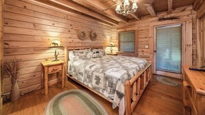 A cabin-style bedroom with wooden walls and ceiling, a bed with a checkered blanket, two bedside tables with lamps, and a window with blinds. - Great rates-2B-2B cabin by Fall Creek Falls-Amazing views with hot tub&fire pit  (Spencer)