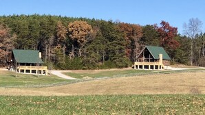 Two cabins with green roofs, surrounded by a grassy field and a forested hillside. - Great rates-2B-2B cabin by Fall Creek Falls-Amazing views with hot tub&fire pit  (Spencer)