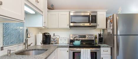 A kitchen with white cabinets, stainless steel appliances, a granite countertop, and a blue kettle.