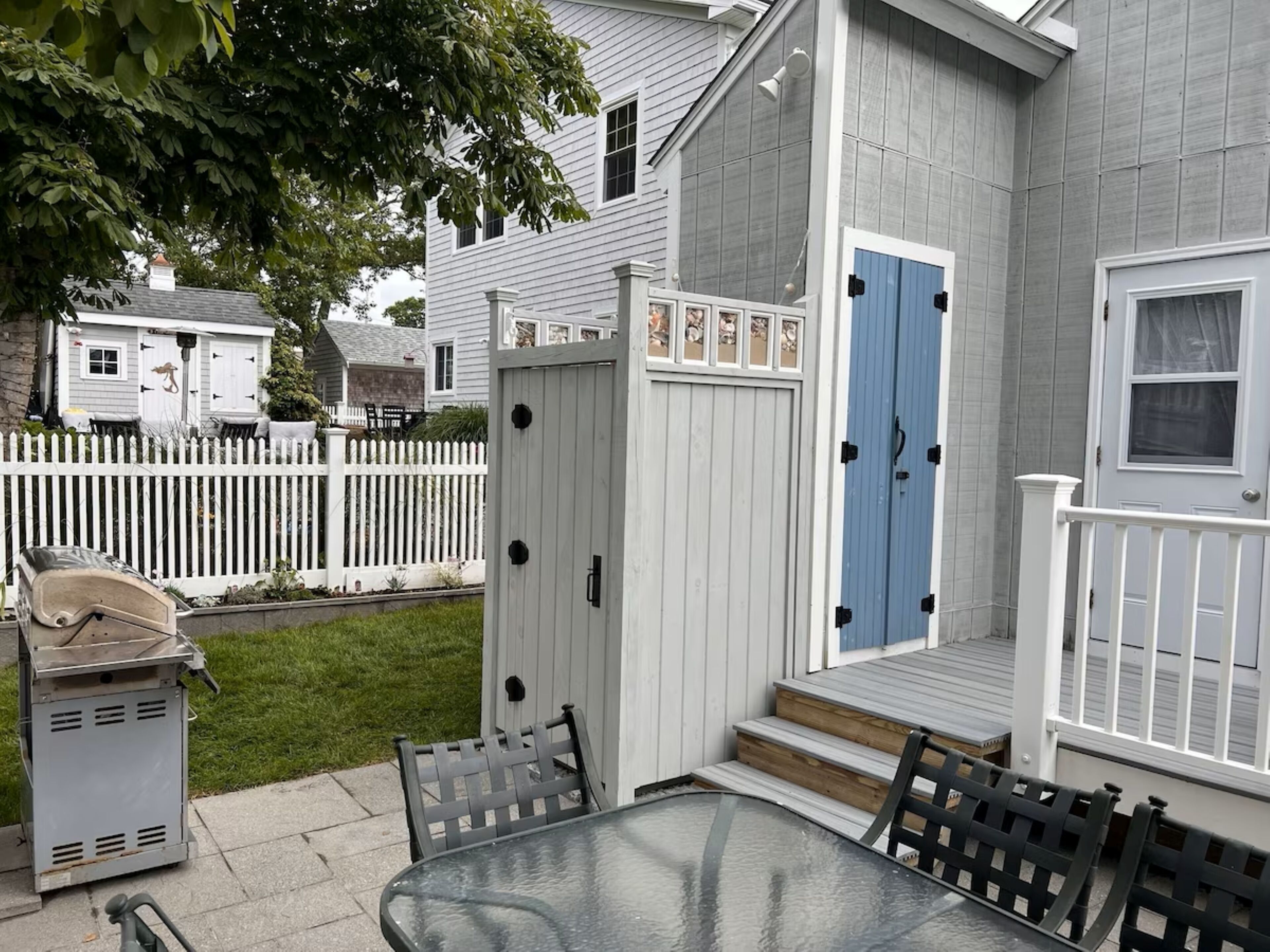 A patio area with a glass table and chairs, a white fence, and a blue door.