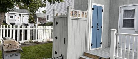 A patio area with a glass table and chairs, a white fence, and a blue door.