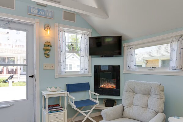 Ein Zimmer mit Fernseher, Kamin, einem Schild im Strandstil und einem Fenster mit Vorhängen.