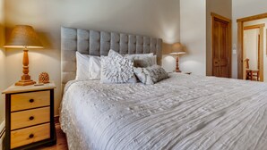 A neatly made bed with a tufted headboard, two bedside tables with lamps, and a wooden door in the background. - 4 Bedroom Penthouse Condo w Gondola Mountain access! Walk to Ski, Shop or Dine! (Keystone)