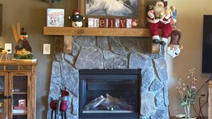 A cozy living room with a stone fireplace, a Christmas wreath, a painting of a skier, and a shelf with holiday decorations. - 4 Bedroom Penthouse Condo w Gondola Mountain access! Walk to Ski, Shop or Dine! (Keystone)