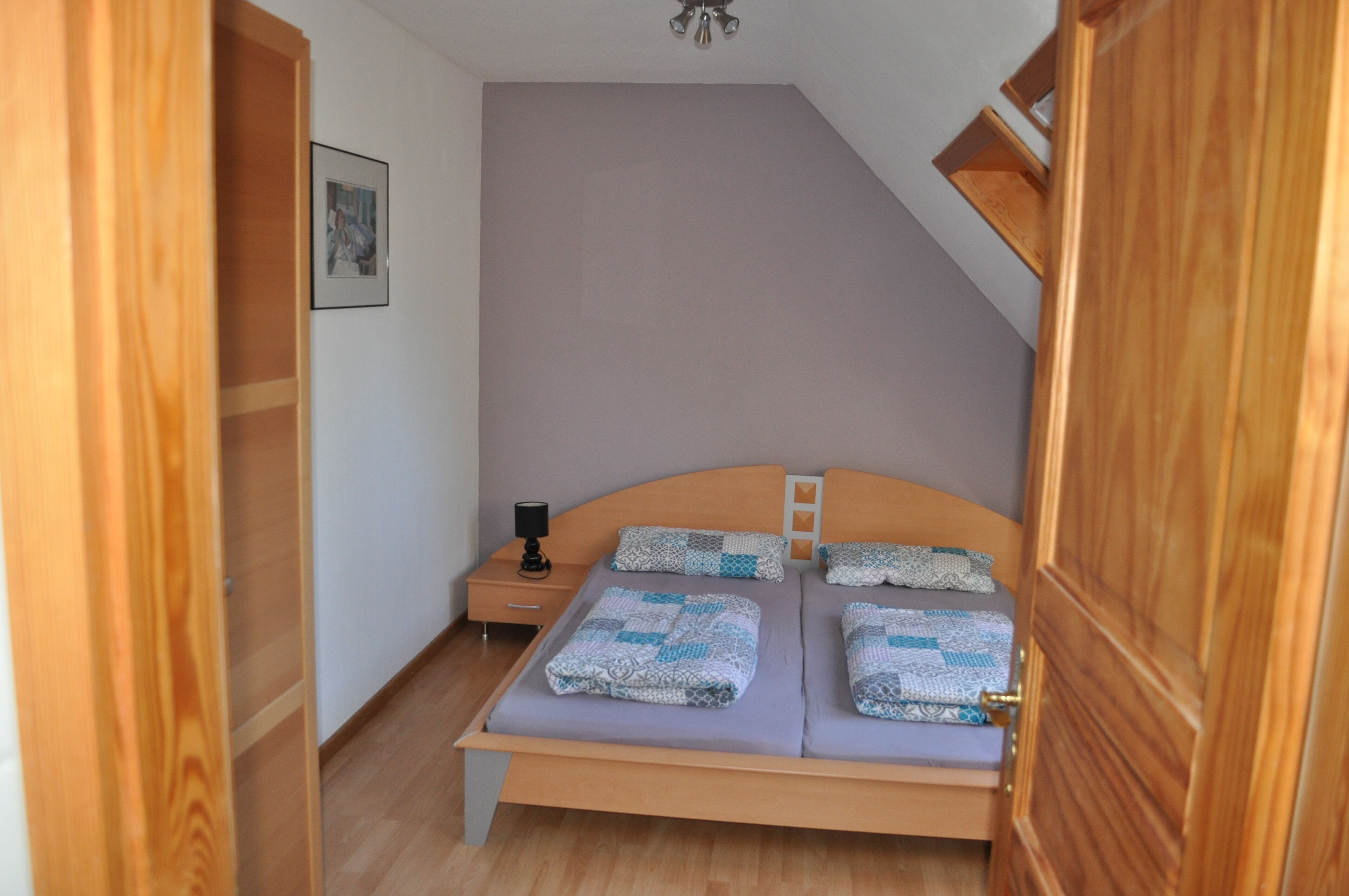 Ein Schlafzimmer mit einem hölzernen Bett, einem Nachttisch und einem gerahmten Bild an der Wand.