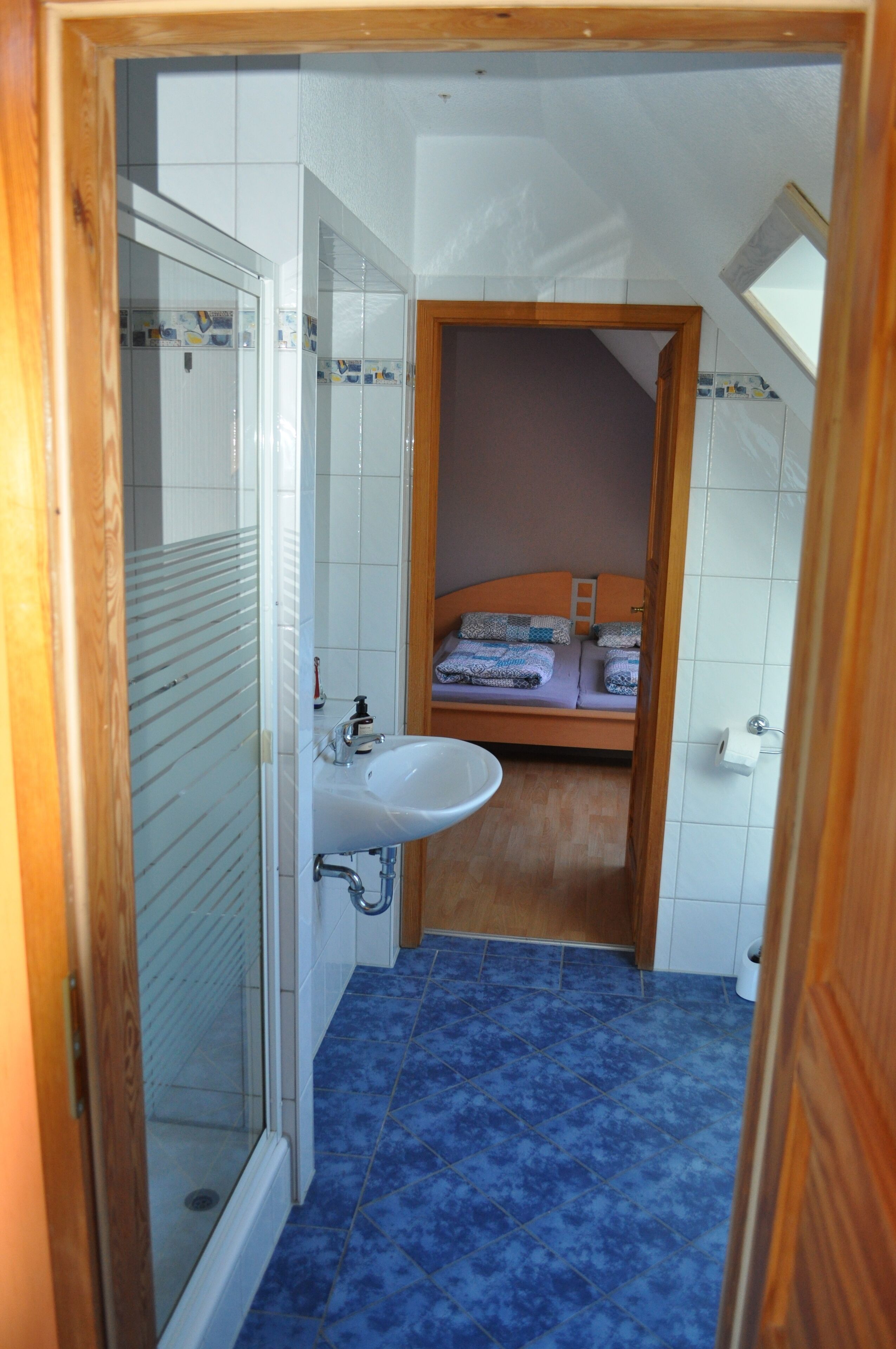 A compact bathroom with a shower, sink, and a small bed area.