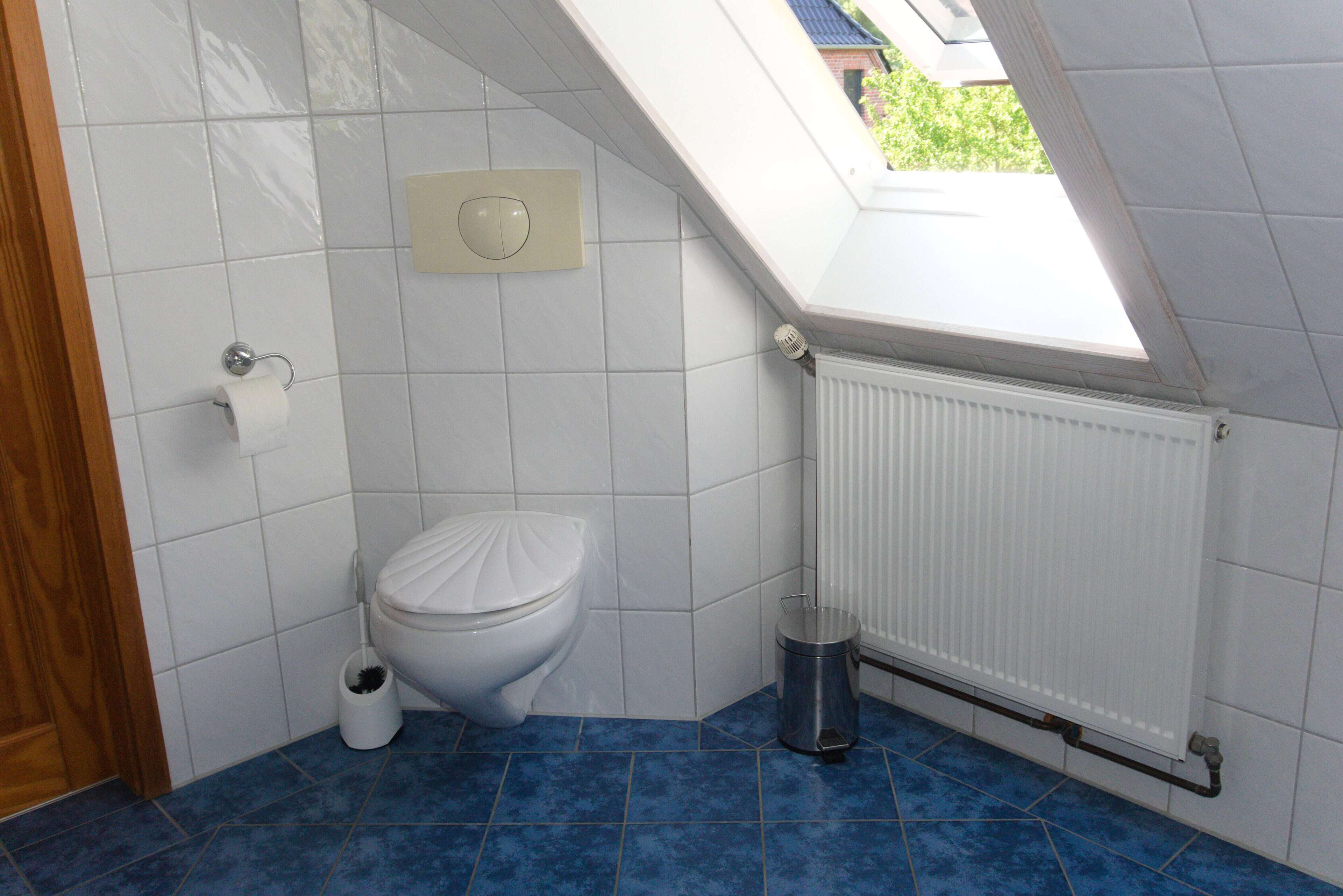 Une petite salle de bain moderne avec un puits de lumière, des carreaux blancs, des toilettes, un radiateur et une poubelle.