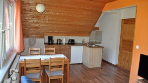 Een compacte keuken met houten balken in het plafond, een eethoek met een tafel en stoelen, en een klein schiereiland met een spoelbak.