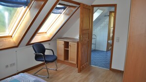 Een kamer met een schuine kap, dakramen, een blauwe stoel, een houten kast en een badkamer die door een open deur zichtbaar is.