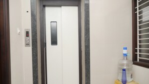 An elevator with a digital display, a water dispenser, and a yellow stool. - Kubera Service Apartments (Tiruchirappalli)