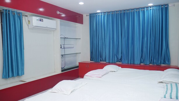 A hotel room with a bed, a red wardrobe, a white air conditioning unit, and blue curtains. - Kubera Service Apartments (Tiruchirappalli)