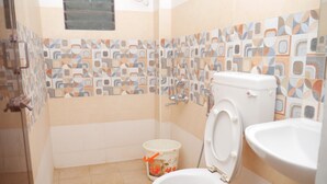 A bathroom with a toilet, sink, and tiled walls. - Kubera Service Apartments (Tiruchirappalli)