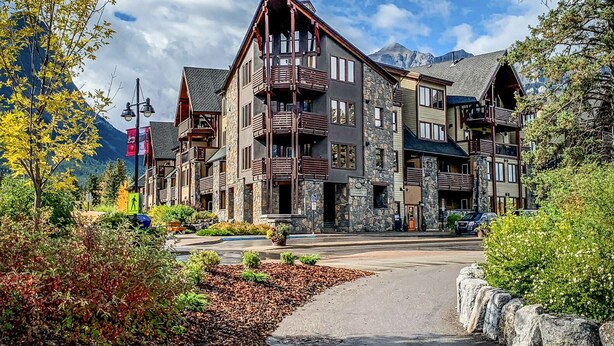 A multi-story lodge with stone and wood exterior, balconies, and a mountain backdrop.