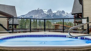 A hot tub with a mountain view, surrounded by wooden buildings and a metal railing.