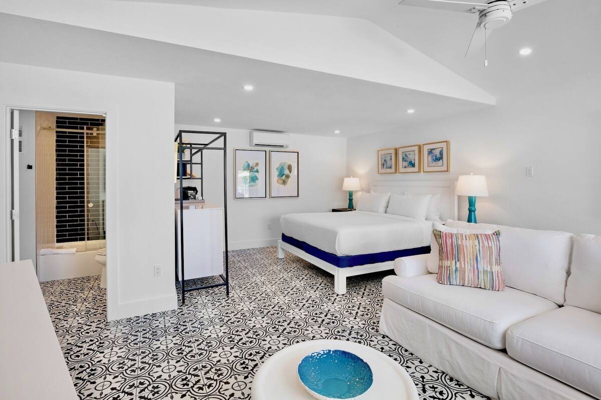 A modern hotel room with a bed, a sofa, a bathroom, and a ceiling fan.