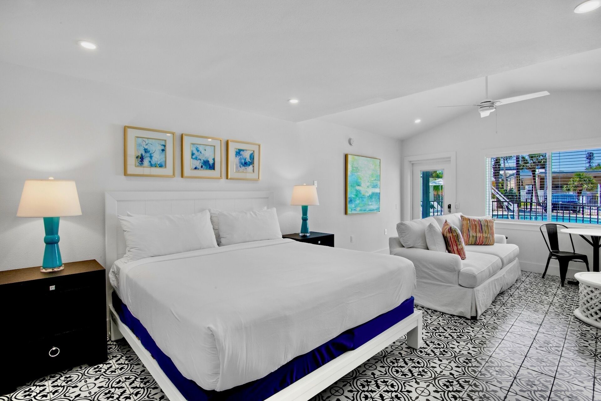 A hotel room with a large bed, a sofa, a dining table, and artwork on the walls.