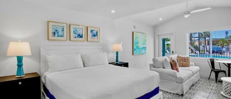 A hotel room with a large bed, a sofa, a dining table, and artwork on the walls.