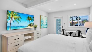 A bedroom with a large bed, a desk with a chair, a TV on the wall, and a window with a view of palm trees. - Pelican Post at Anna Maria Island Inn (Bradenton Beach)