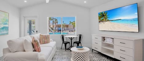 A modern living room with a white sofa, a dining table with chairs, a TV mounted on the wall, and a patterned floor.