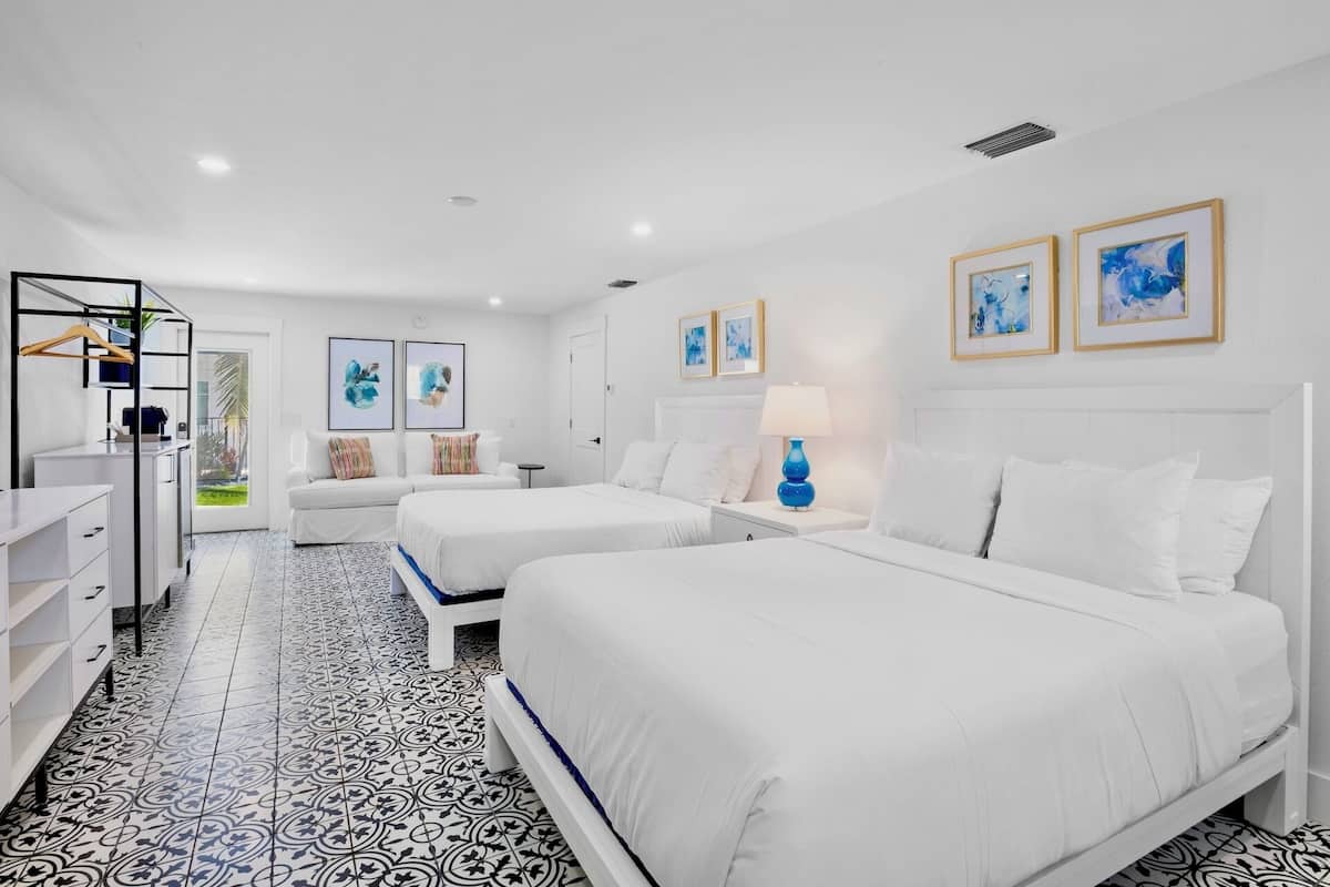 A hotel room with two beds, a desk, and a chair. There are two framed pictures on the wall.