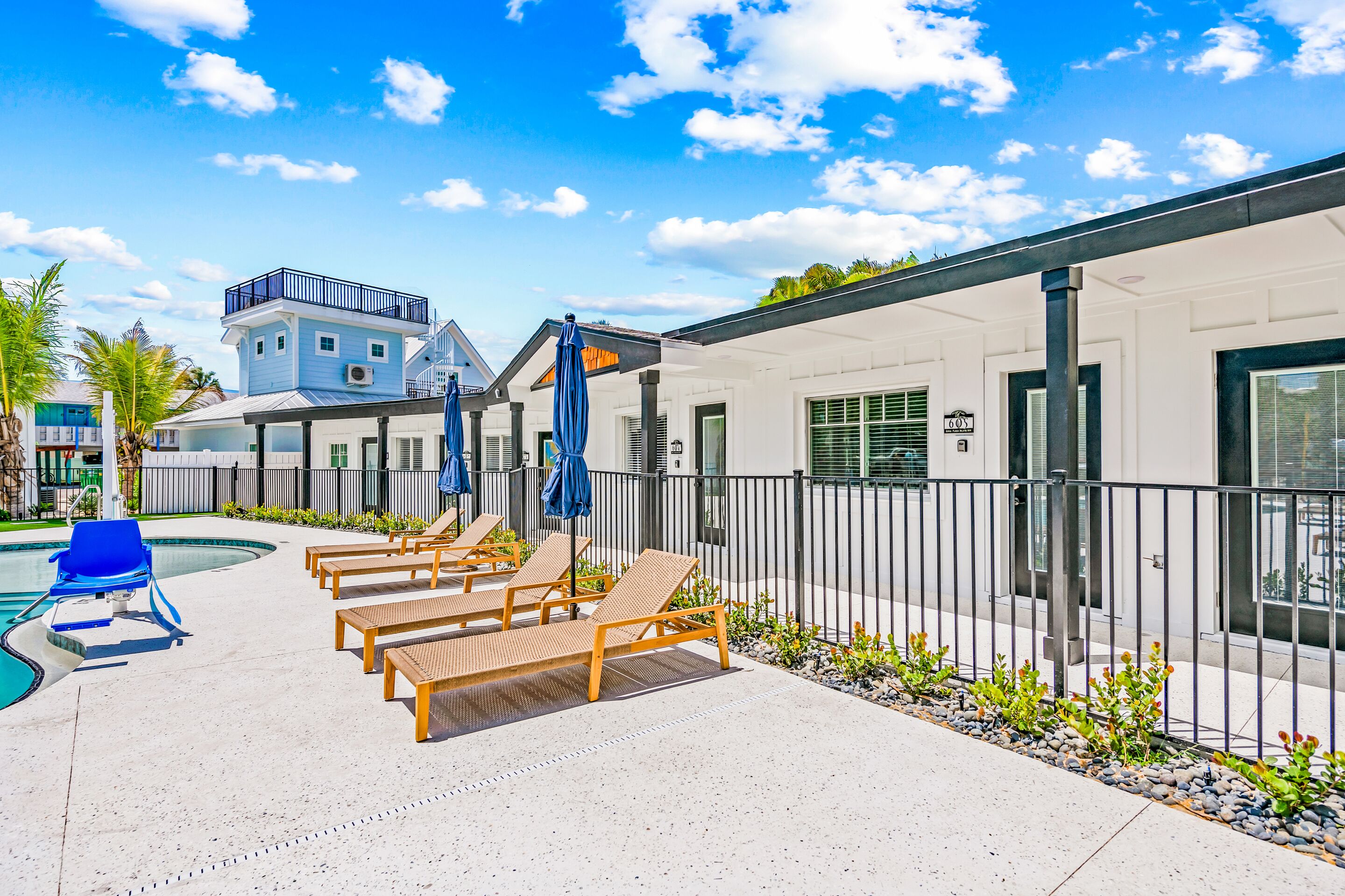 A pool area with lounge chairs and umbrellas, a building with a balcony, and a clear sky.