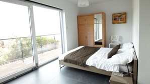 A modern bedroom with a large sliding glass door leading to a balcony, a bed with white bedding and a brown throw, a wooden wardrobe, and a small white chair. - Maremuntagna lux. villa sea view 7 bed swim. pool 10min city (Porto-Vecchio)
