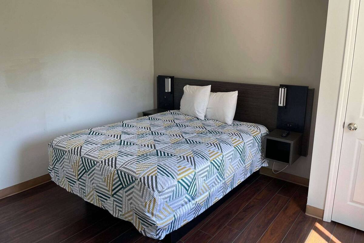 Un dormitorio con cama, mesita de noche, televisión y una puerta.