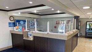 A reception desk with a glass partition, a clock on the wall, and a blue mat in front. - Studio 6 Peoria, IL (Peoria)