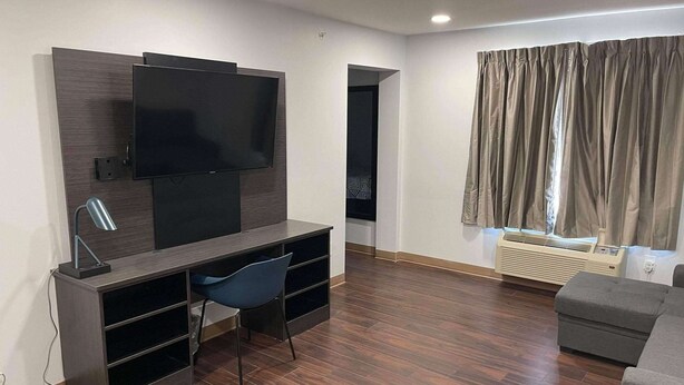 A modern living room with a flat-screen TV mounted on a dark wood wall, a blue chair, a grey sofa, and a window with curtains. - Studio 6 Peoria, IL (Peoria)