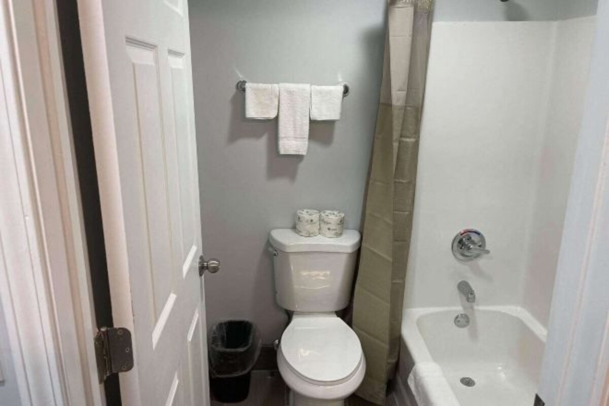 A bathroom with a toilet, a sink, and a shower. There are two rolls of toilet paper on the toilet tank.