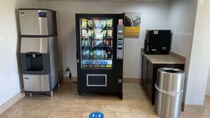A vending machine with a variety of drinks, a water dispenser, and a trash can in a clean, tiled room. - Studio 6 Peoria, IL (Peoria)