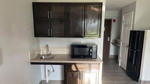 A kitchen with dark wooden cabinets, a stainless steel sink, a black microwave, and a black refrigerator. - Studio 6 Peoria, IL (Peoria)