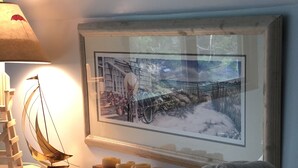 Un meuble-lavabo bien rangé, agrémenté d’un tableau représentant un paysage, d’un bloc de bois décoratif et de serviettes enroulées.