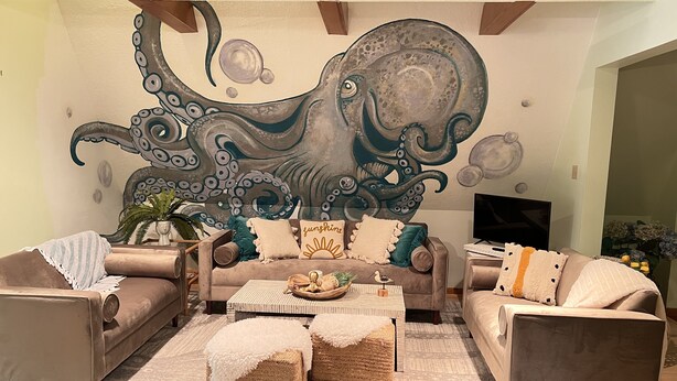 Un salon avec une grande fresque représentant un poulpe sur le mur, deux canapés, une table basse et un téléviseur.